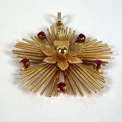 A yellow gold floral sunburst pendant with rubies, on a white background