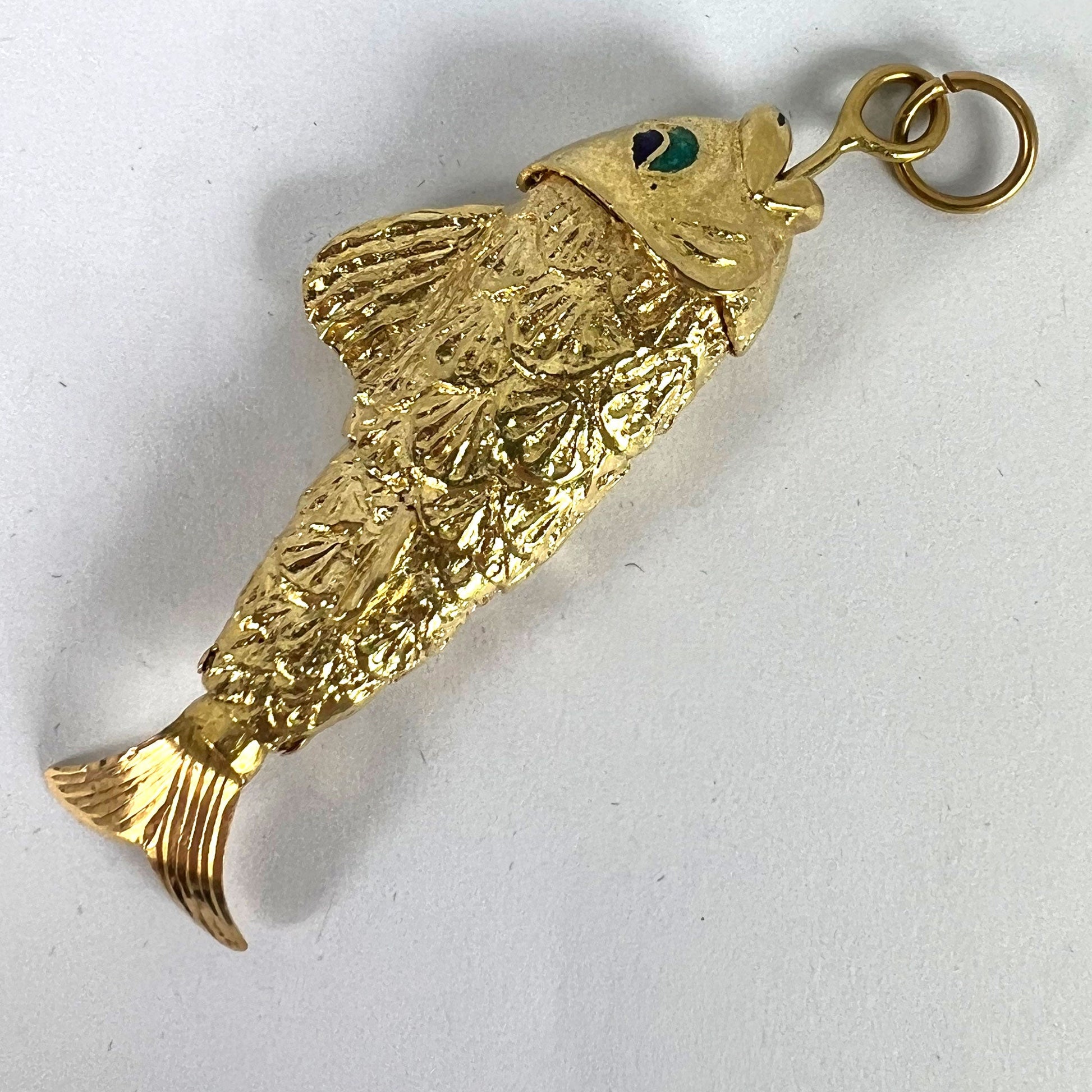 A yellow gold fish pendant with a green eye, on a white background