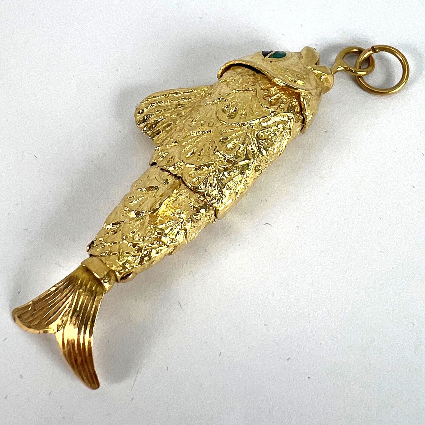 A yellow gold fish pendant with a green eye, on a white background