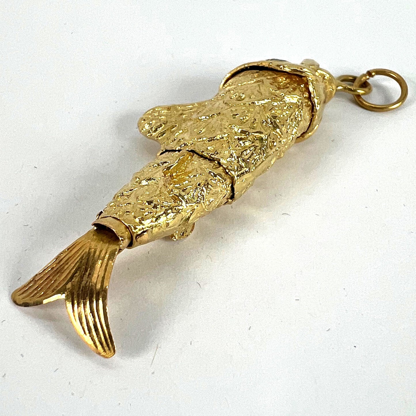 A yellow gold fish pendant with a green eye, on a white background