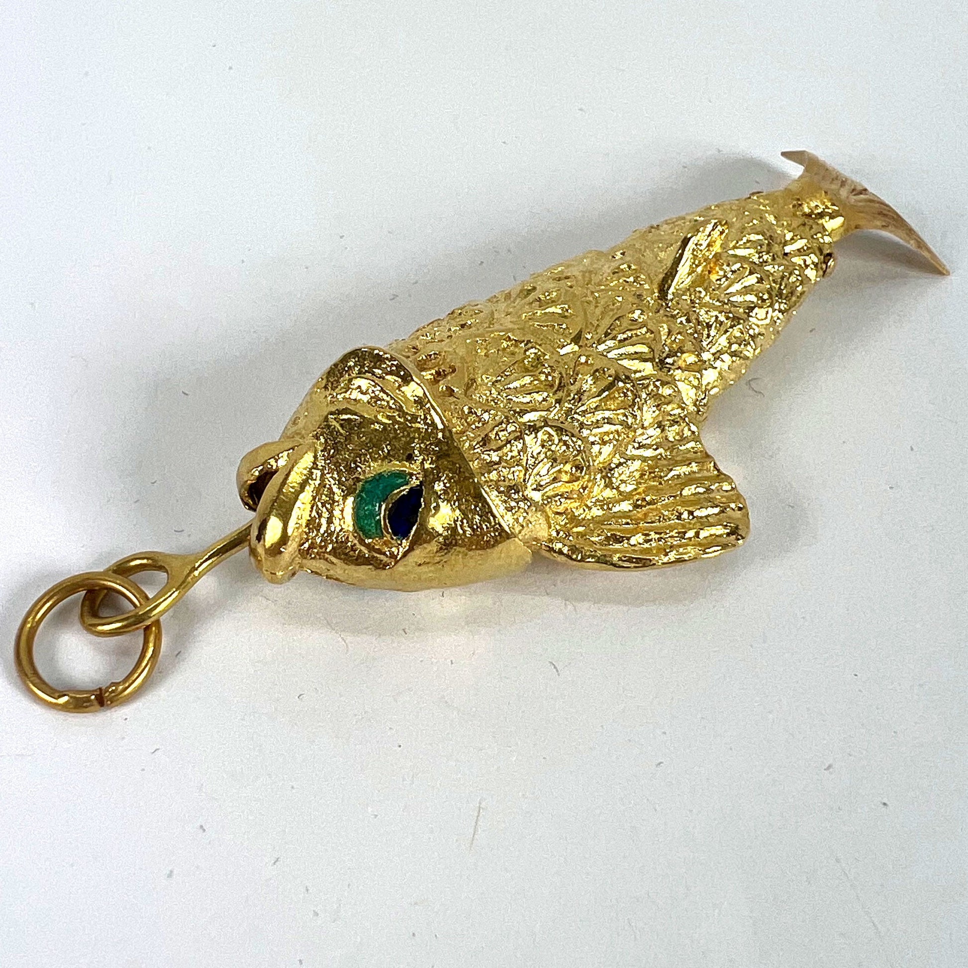 A yellow gold fish pendant with a green eye, on a white background