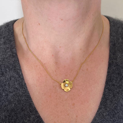 A yellow gold and diamond flower pendant necklace, modelled by a woman