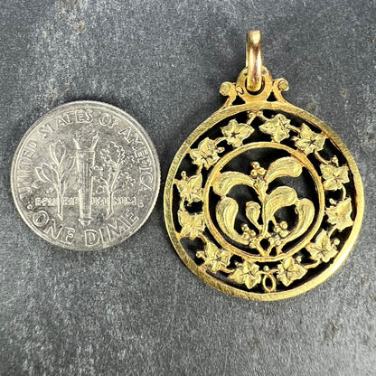 A round yellow gold pendant with mistletoe and ivy leaves, next to a dime coin