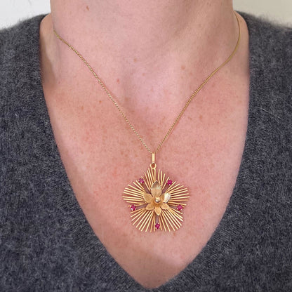 A yellow gold floral sunburst pendant with rubies, modelled on a gold chain