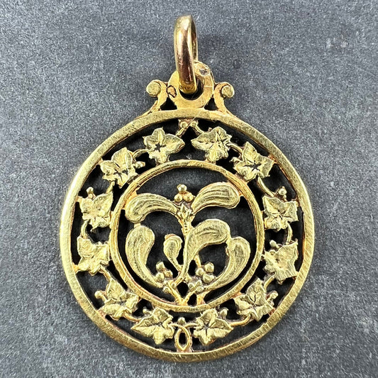 A round yellow gold pendant with mistletoe and ivy leaves, on a grey background