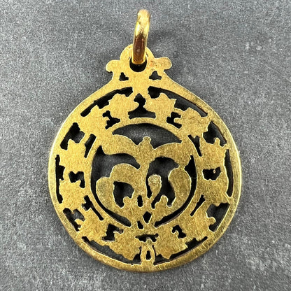 A round yellow gold pendant with mistletoe and ivy leaves, on a grey background