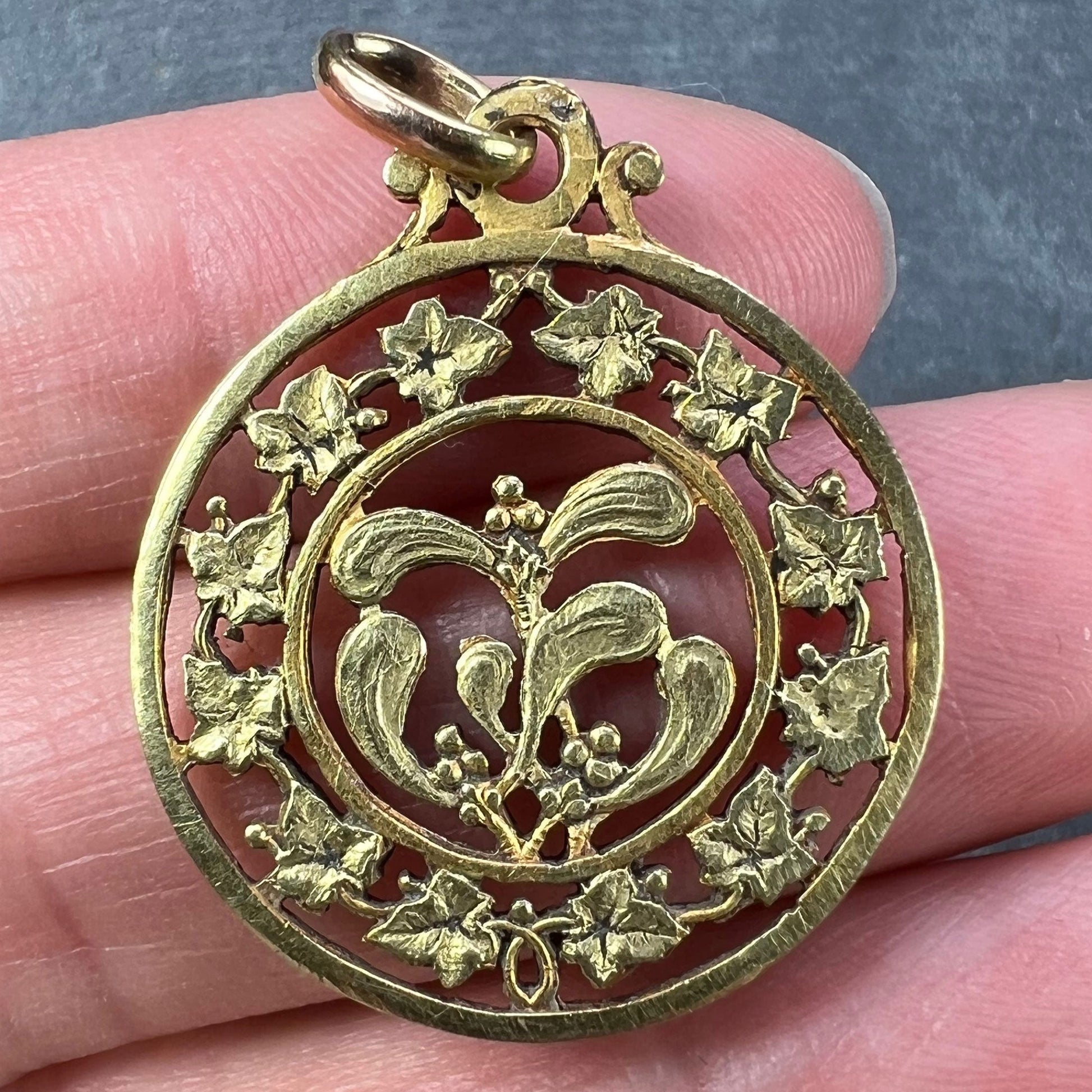 A round yellow gold pendant with mistletoe and ivy leaves, held in a hand