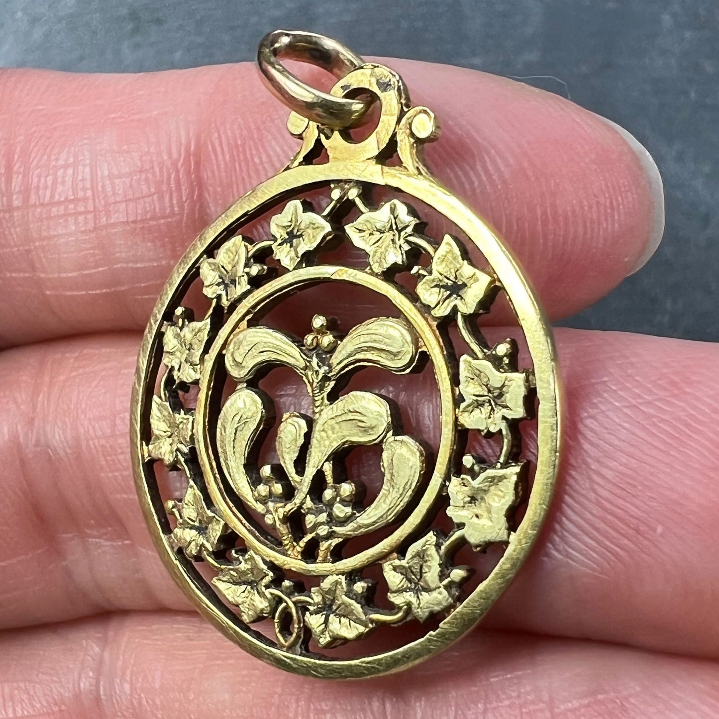 A round yellow gold pendant with mistletoe and ivy leaves, held in a hand