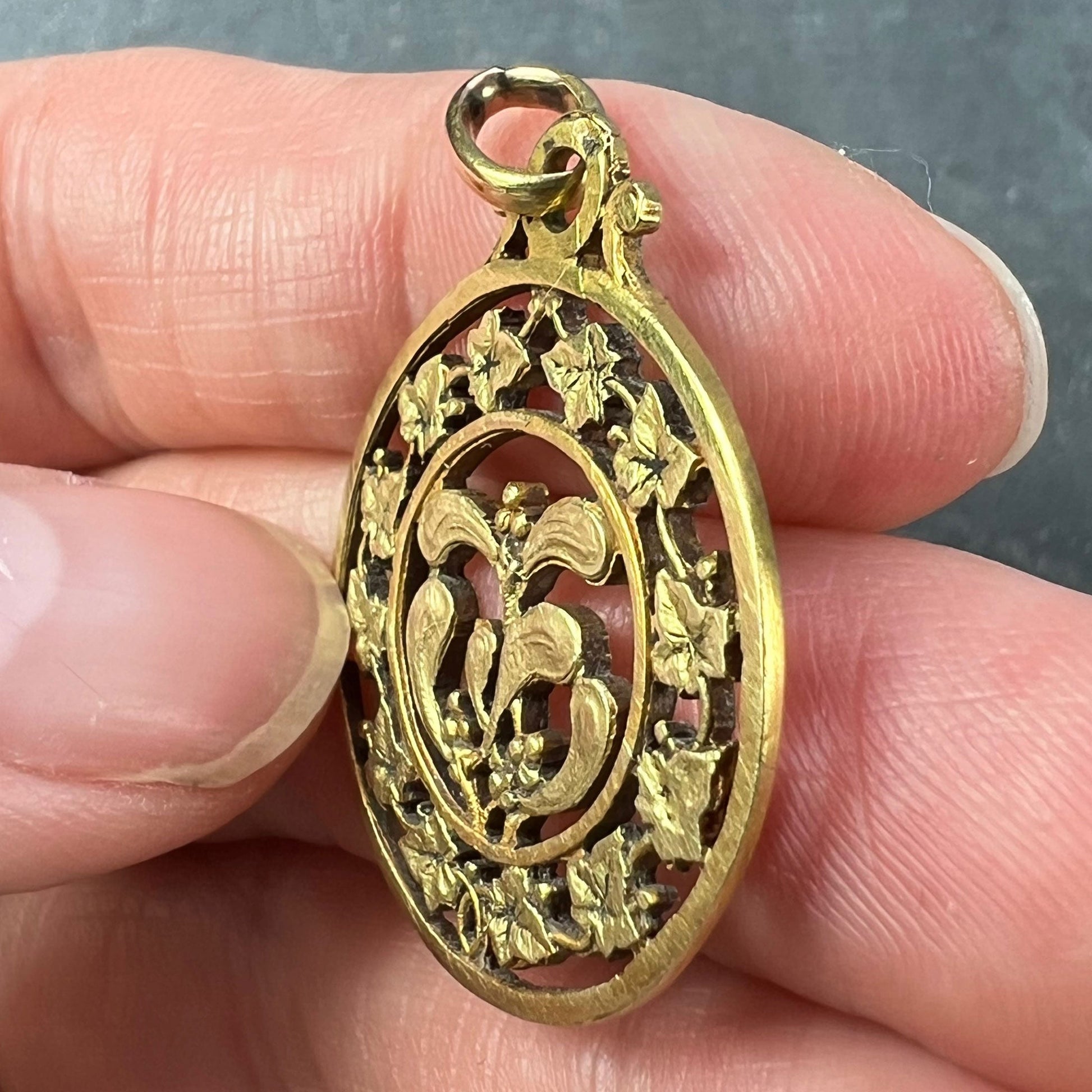A round yellow gold pendant with mistletoe and ivy leaves, held in a hand