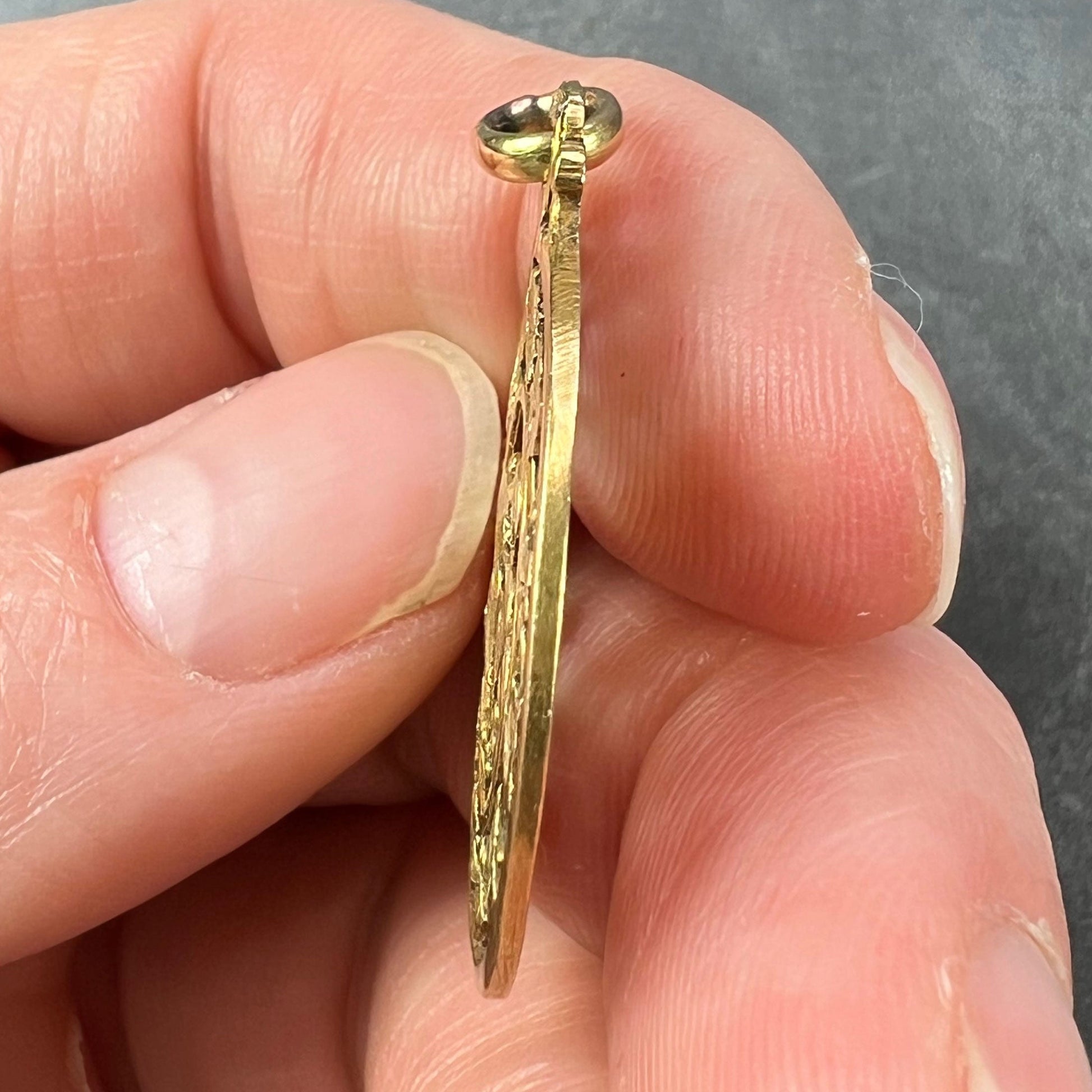 A round yellow gold pendant with mistletoe and ivy leaves, held in a hand