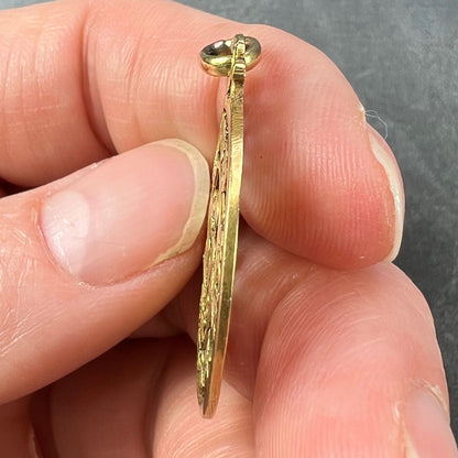 A round yellow gold pendant with mistletoe and ivy leaves, held in a hand