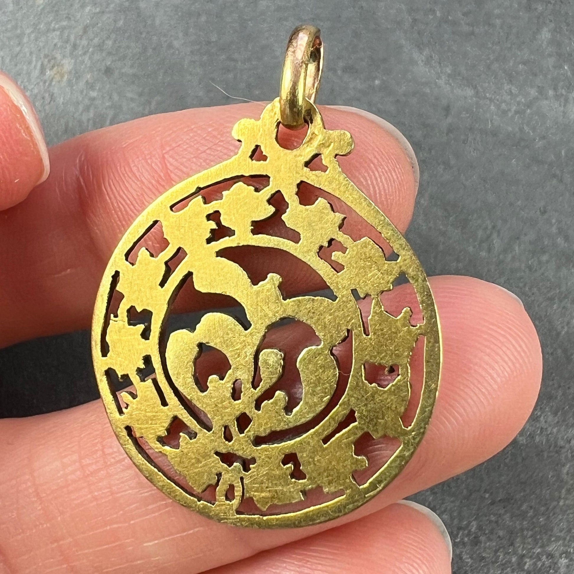 A round yellow gold pendant with mistletoe and ivy leaves, held in a hand