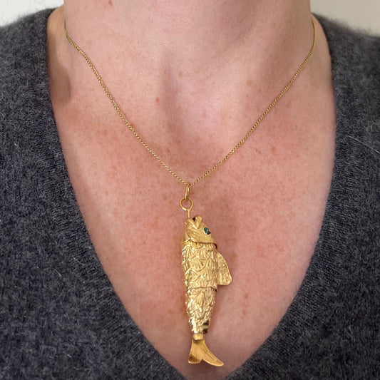 A yellow gold fish pendant with a green eye, modelled on a gold chain