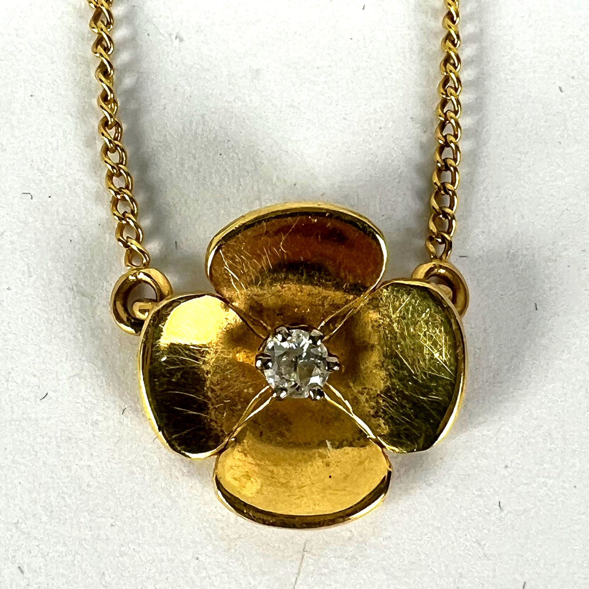 A yellow gold and diamond flower pendant necklace, on a white background