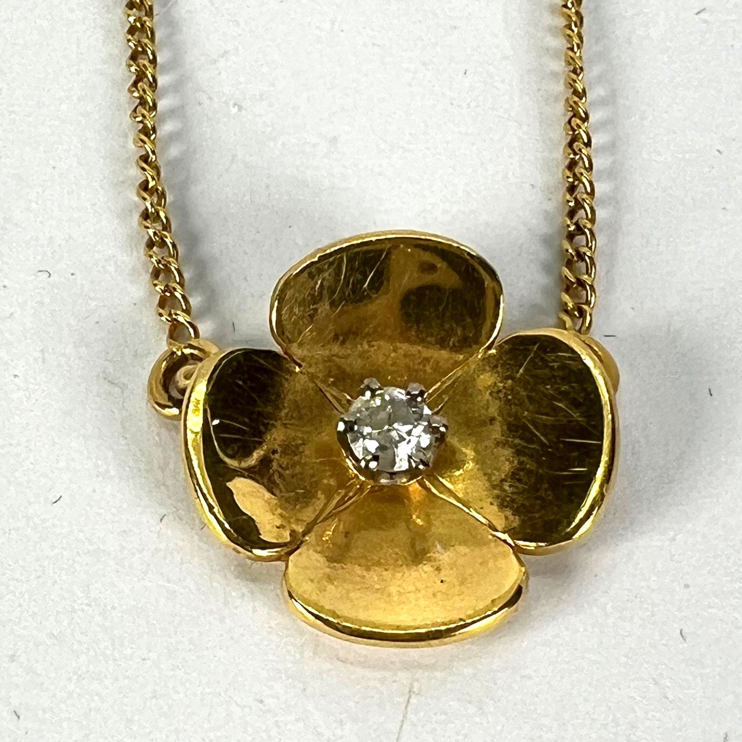 A yellow gold and diamond flower pendant necklace, on a white background