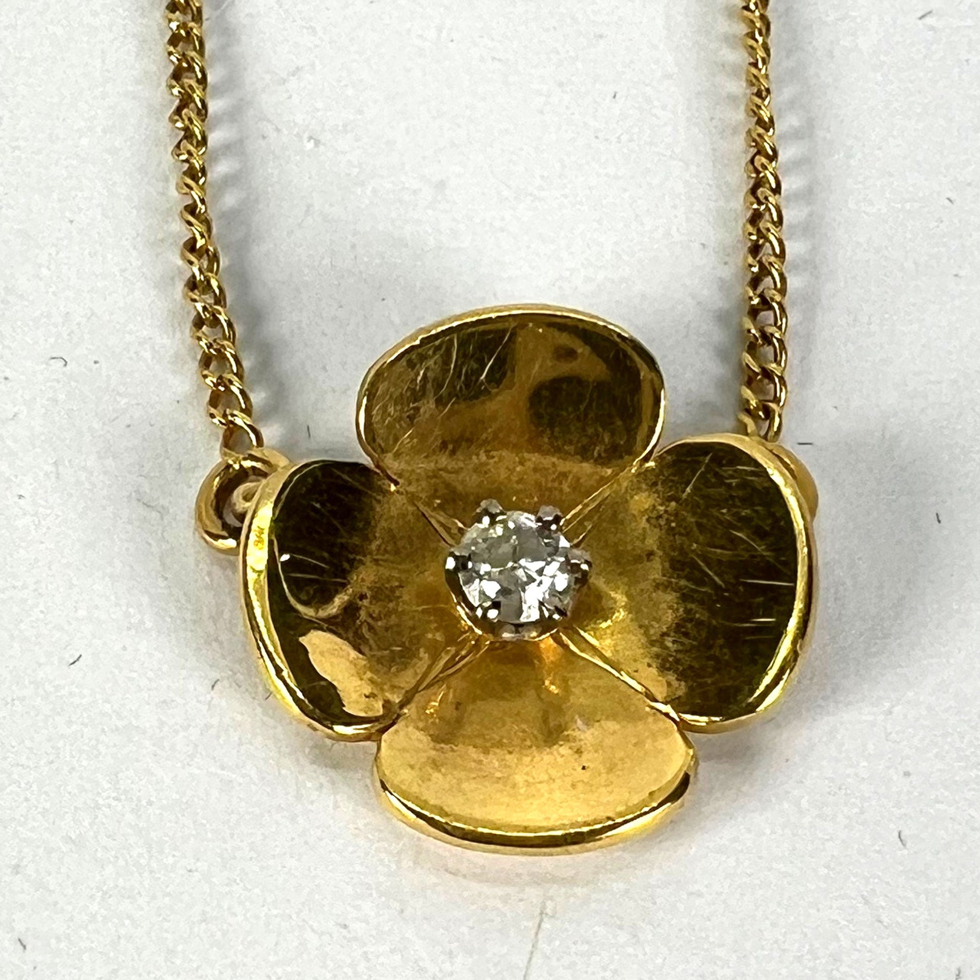 A yellow gold and diamond flower pendant necklace, on a white background