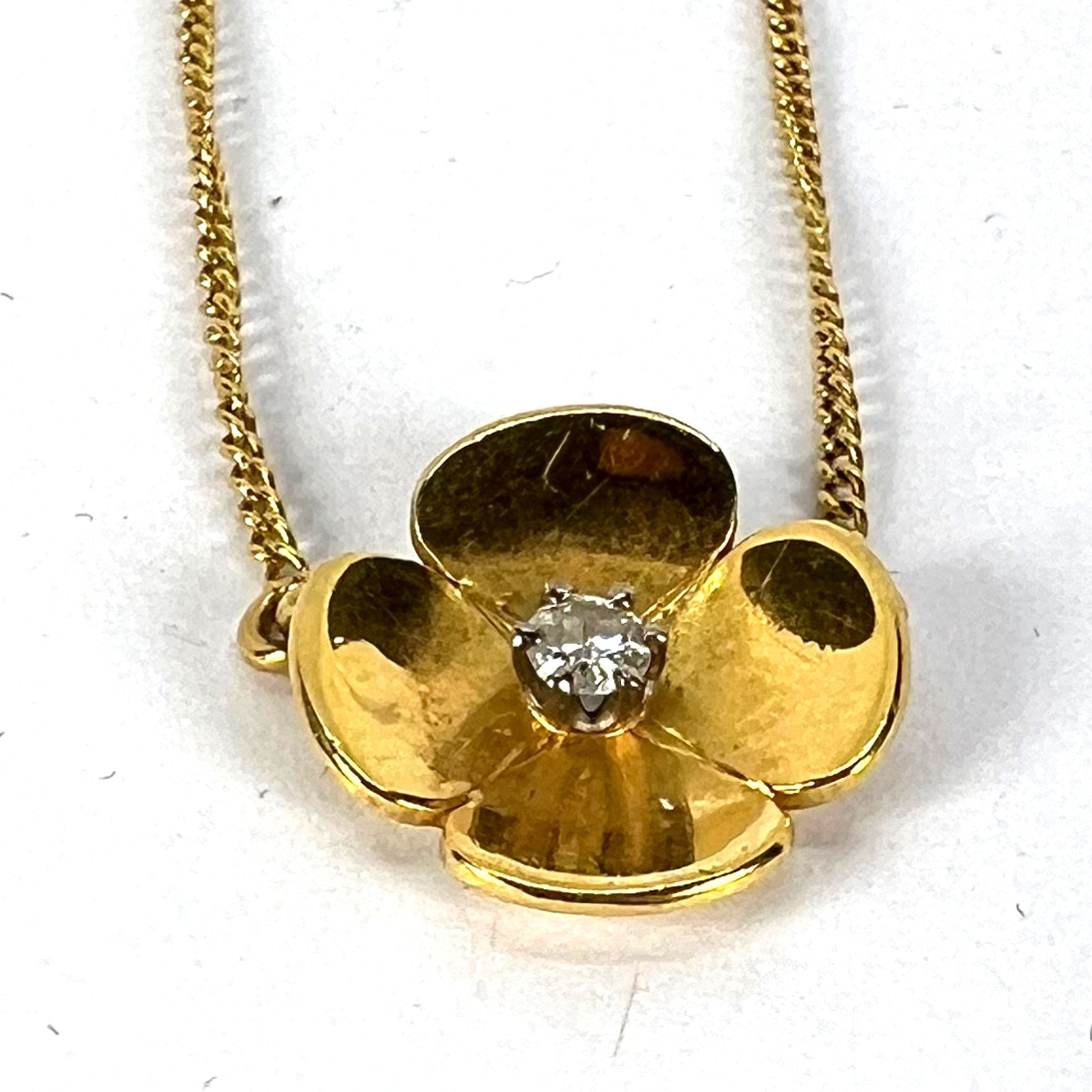 A yellow gold and diamond flower pendant necklace, on a white background