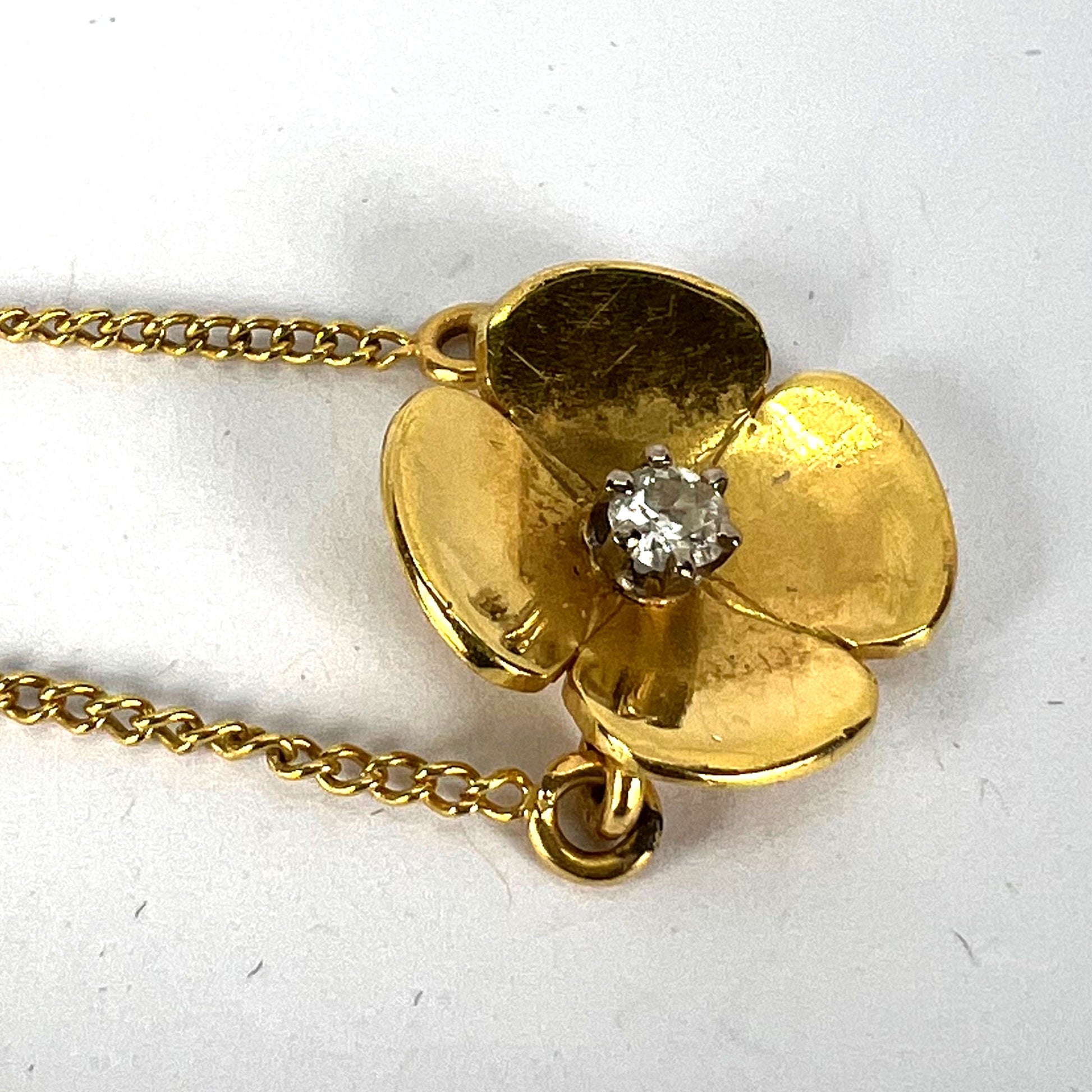 A yellow gold and diamond flower pendant necklace, on a white background