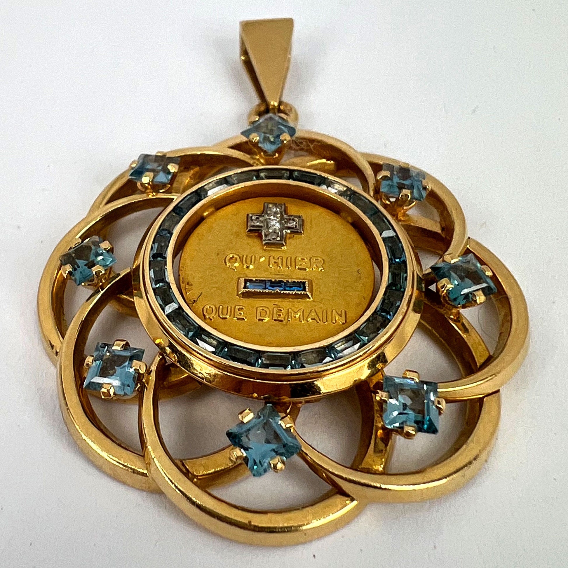 A yellow gold French QU'HIER QUE DEMAIN pendant with blue stones and diamonds, on a white background