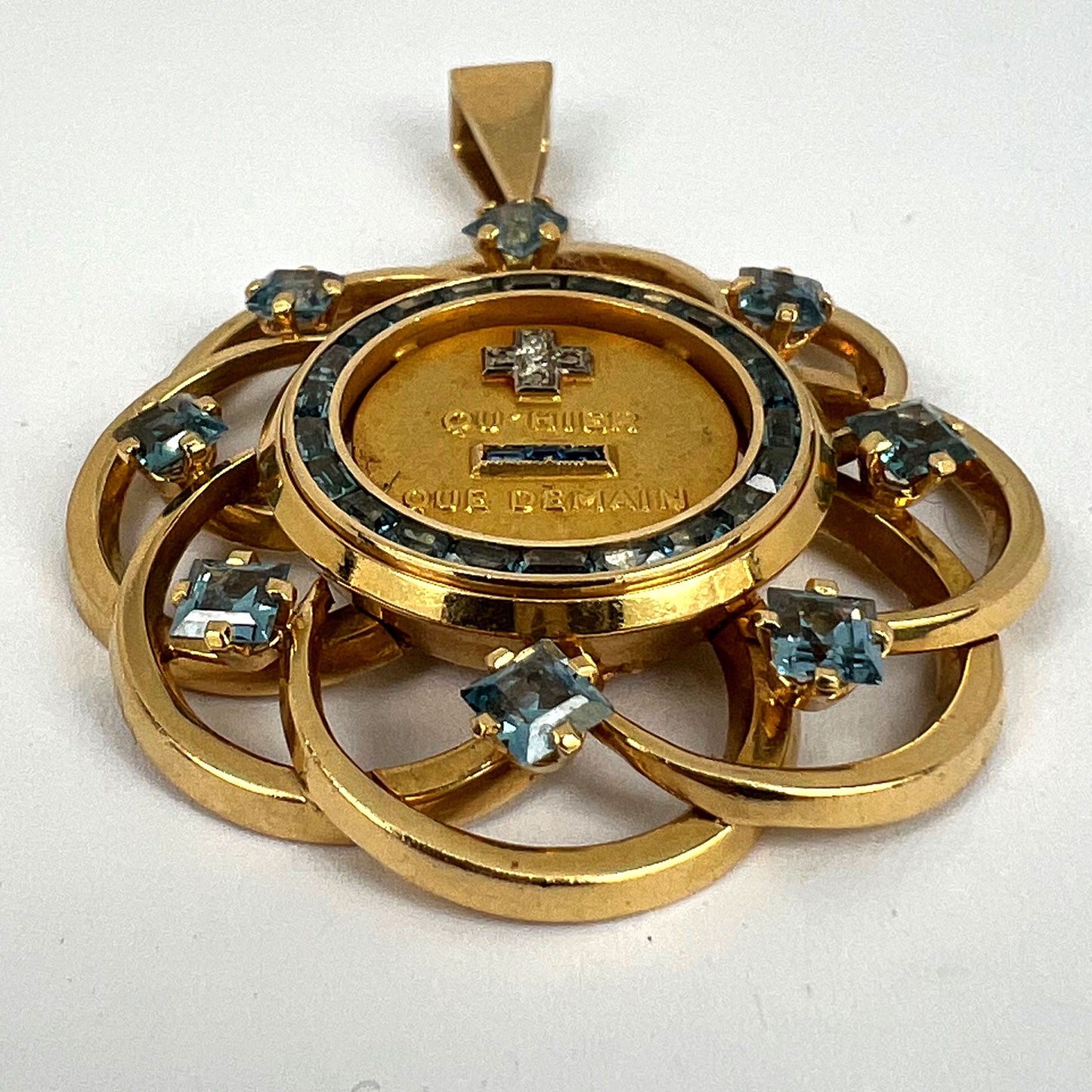 A yellow gold French QU'HIER QUE DEMAIN pendant with blue stones and diamonds, on a white background