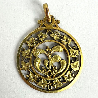 A round yellow gold pendant with mistletoe and ivy leaves, on a white background