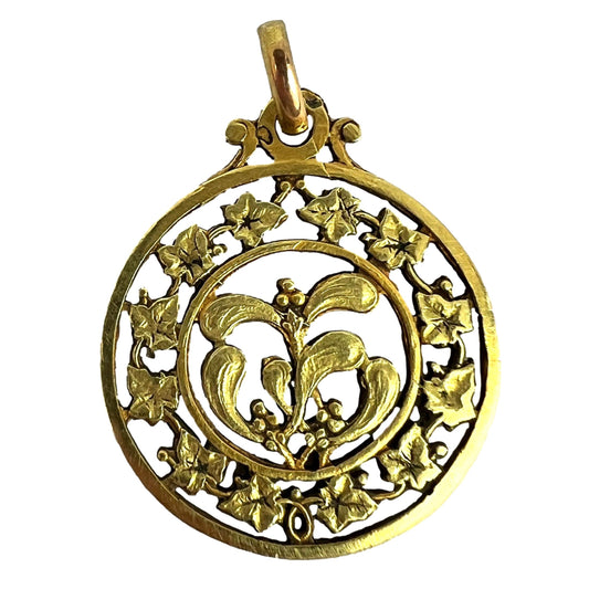 A round yellow gold pendant with mistletoe and ivy leaves, on a white background
