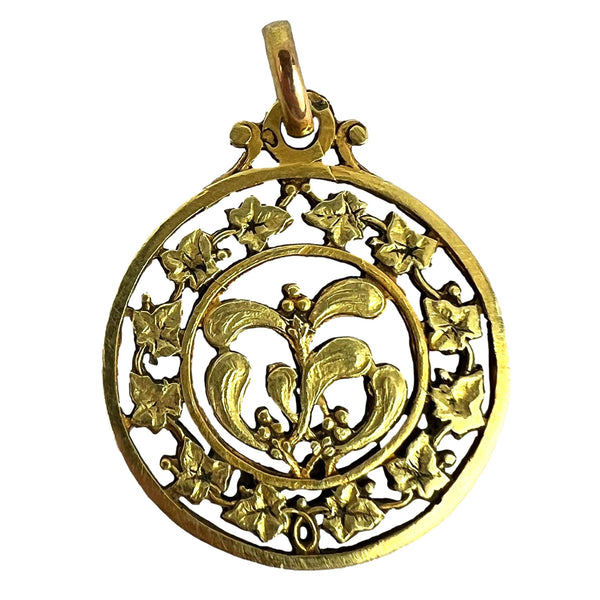 A round yellow gold pendant with mistletoe and ivy leaves, on a white background