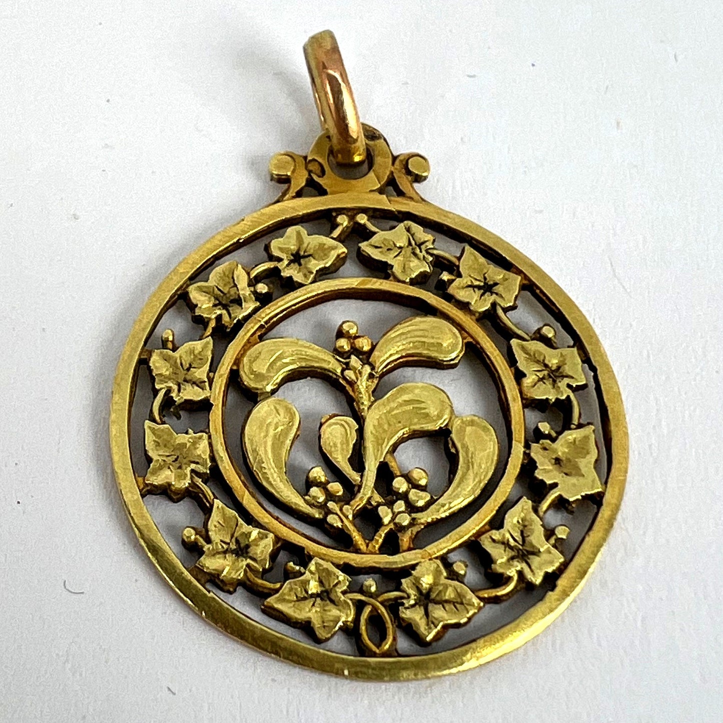 A round yellow gold pendant with mistletoe and ivy leaves, on a white background