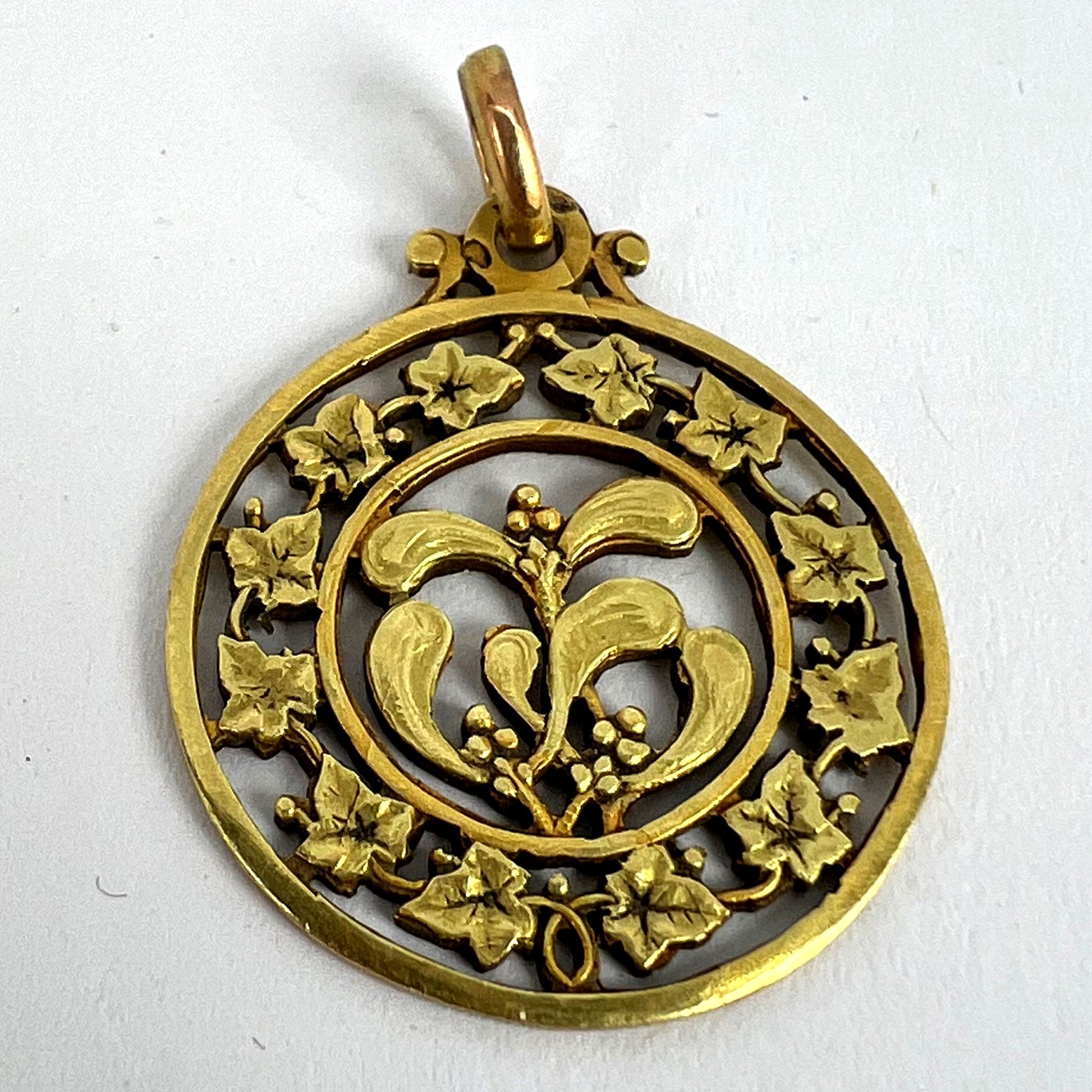 A round yellow gold pendant with mistletoe and ivy leaves, on a white background