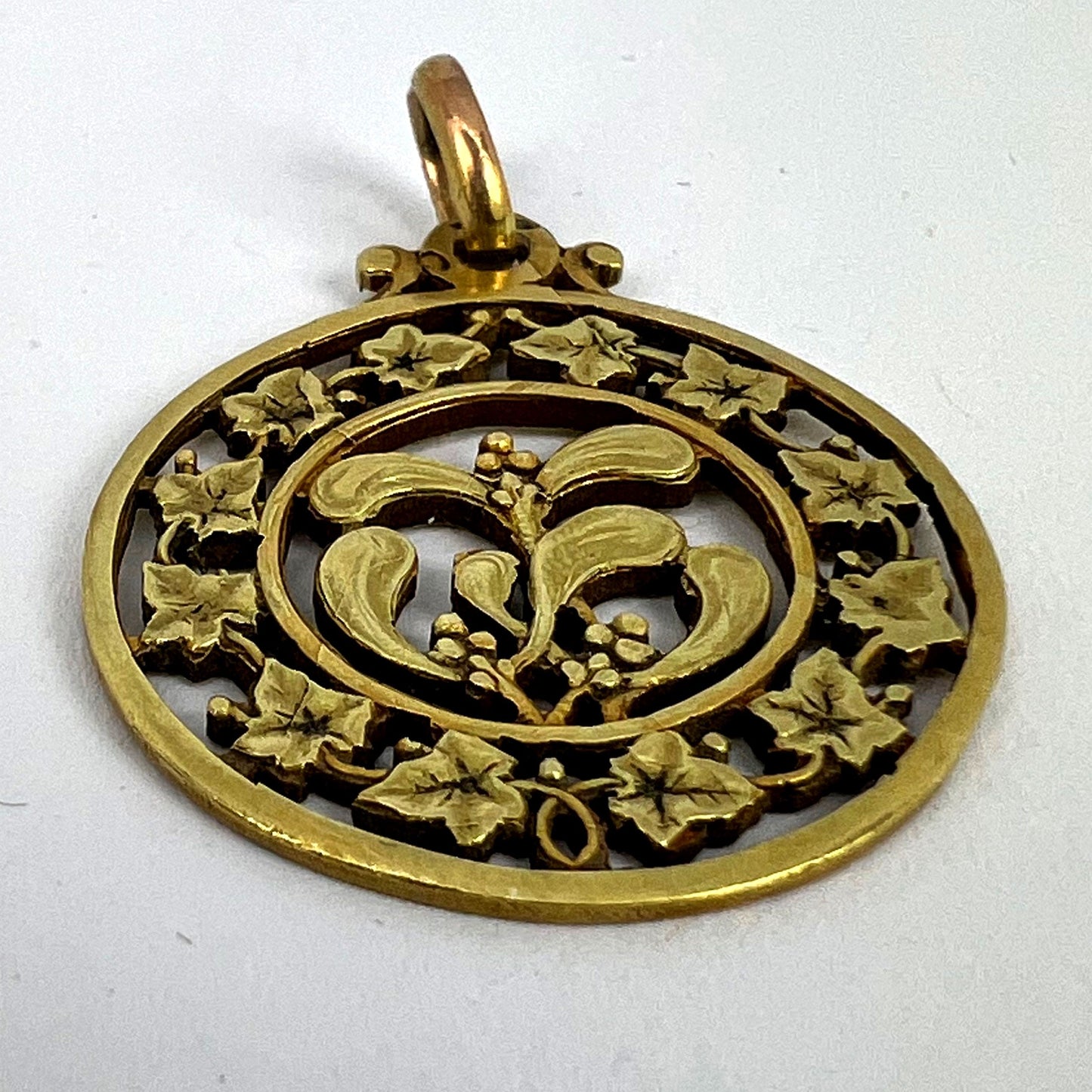 A round yellow gold pendant with mistletoe and ivy leaves, on a white background