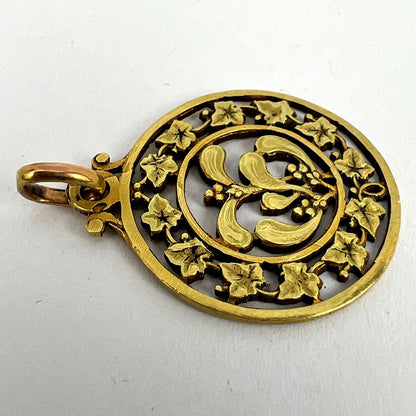 A round yellow gold pendant with mistletoe and ivy leaves, on a white background