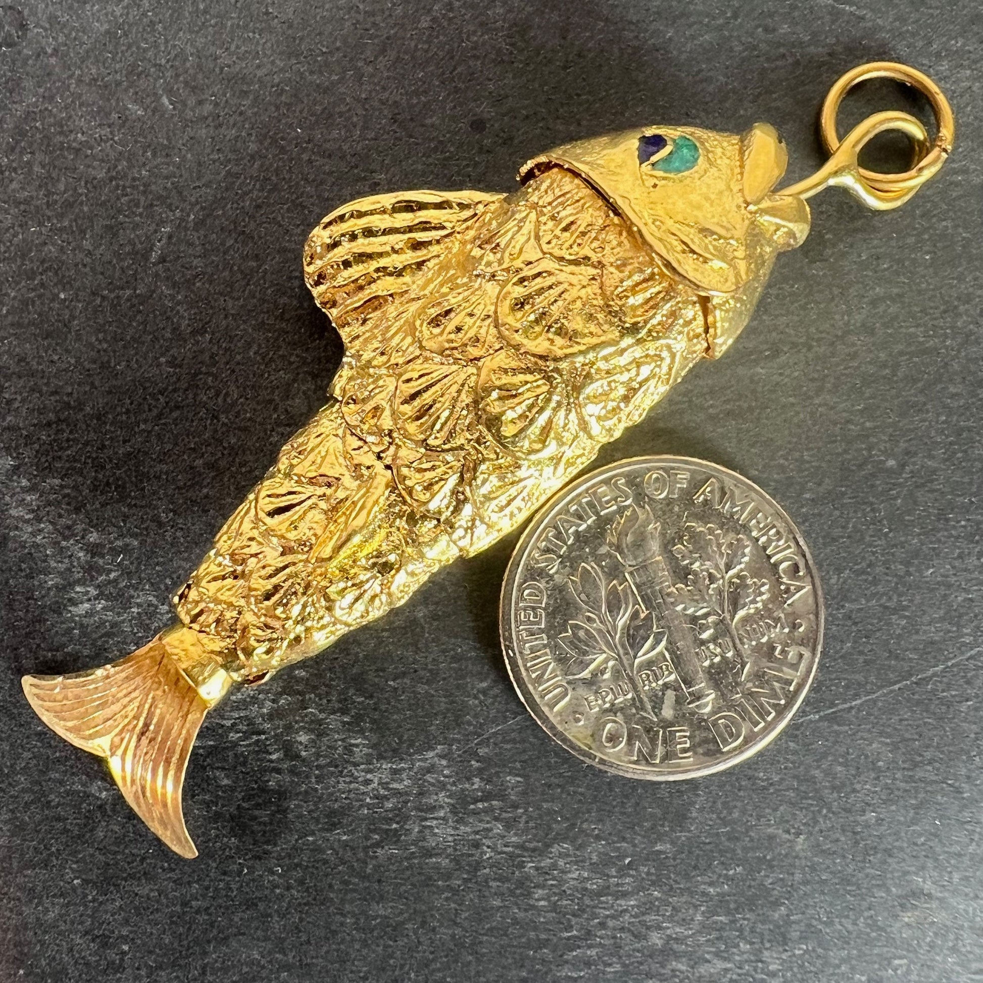 A yellow gold fish pendant with a green eye, next to a dime coin