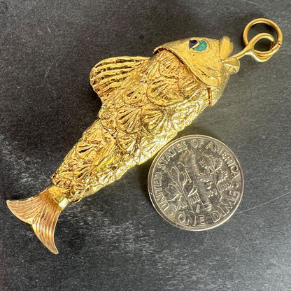 A yellow gold fish pendant with a green eye, next to a dime coin