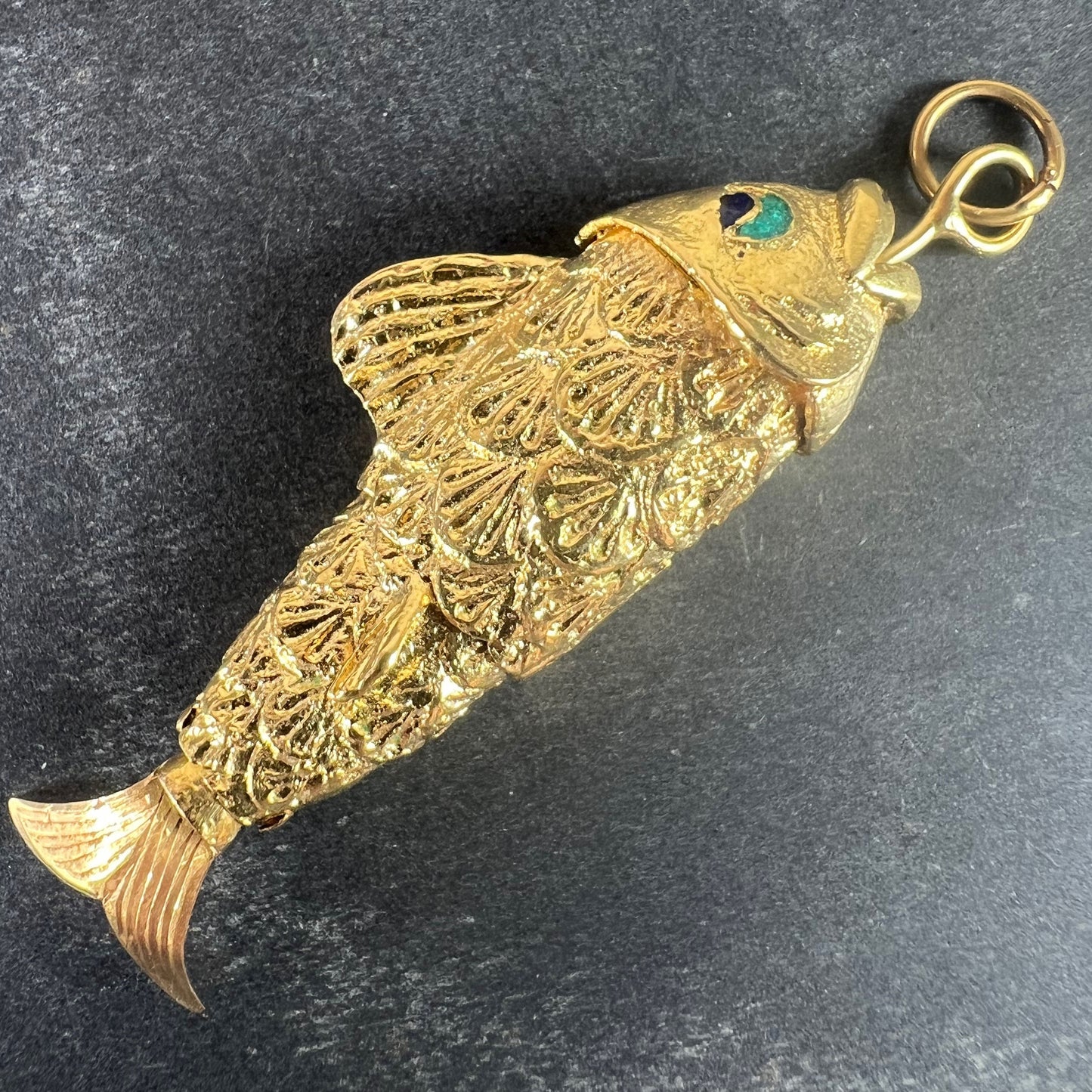 A yellow gold fish pendant with a green eye, on a grey background