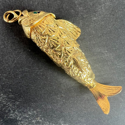 A yellow gold fish pendant with a green eye, on a grey background