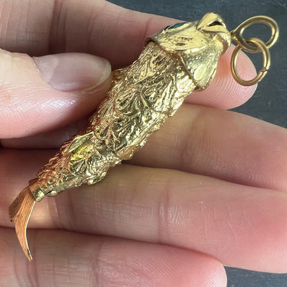 A yellow gold fish pendant with a green eye, held in a hand