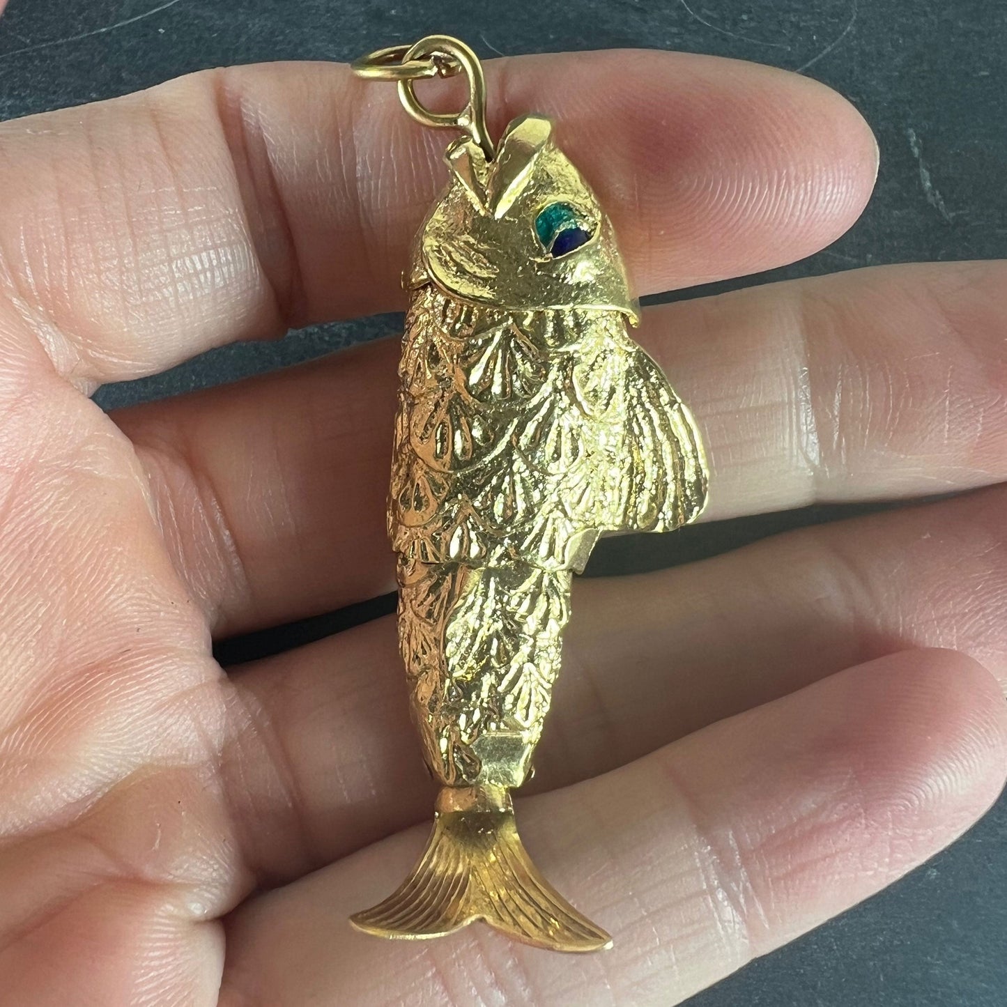 A yellow gold fish pendant with a green eye, held in a hand