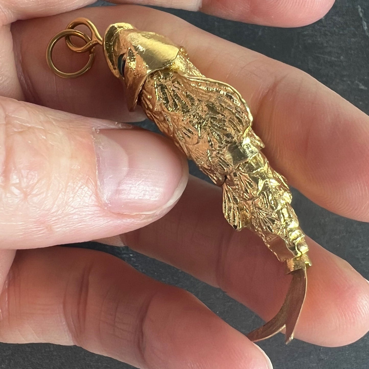 A yellow gold fish pendant with a green eye, held in a hand