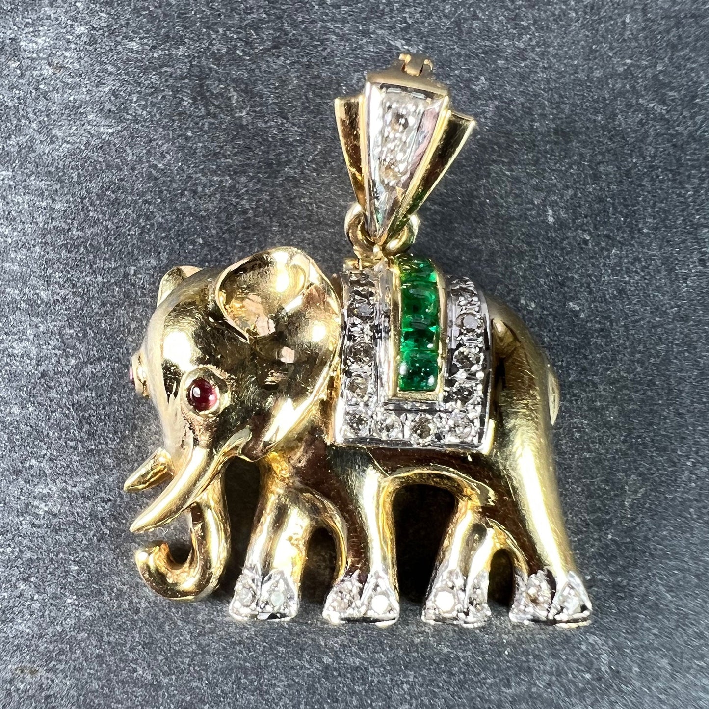 A yellow gold elephant pendant with rubies, emeralds and diamonds, on a grey background