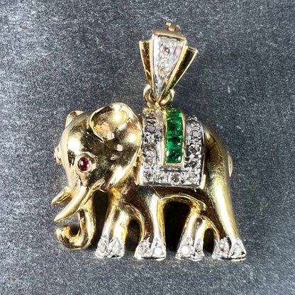A yellow gold elephant pendant with rubies, emeralds and diamonds, on a grey background