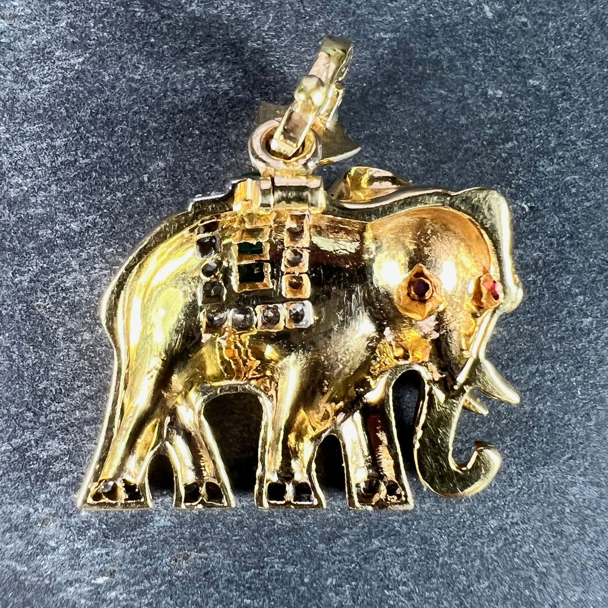 A yellow gold elephant pendant with rubies, emeralds and diamonds, on a grey background