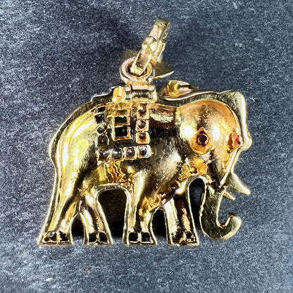 A yellow gold elephant pendant with rubies, emeralds and diamonds, on a grey background