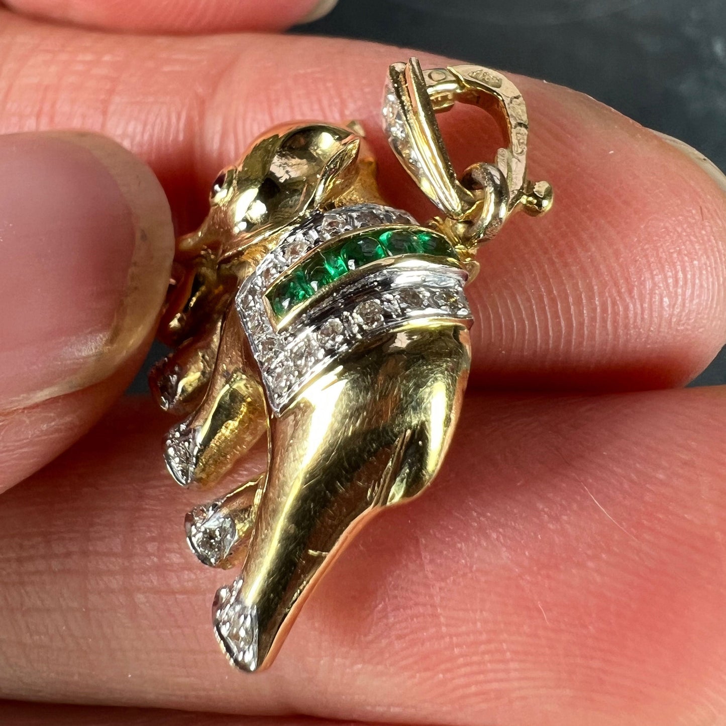 A yellow gold elephant pendant with rubies, emeralds and diamonds, held in a hand on a grey background