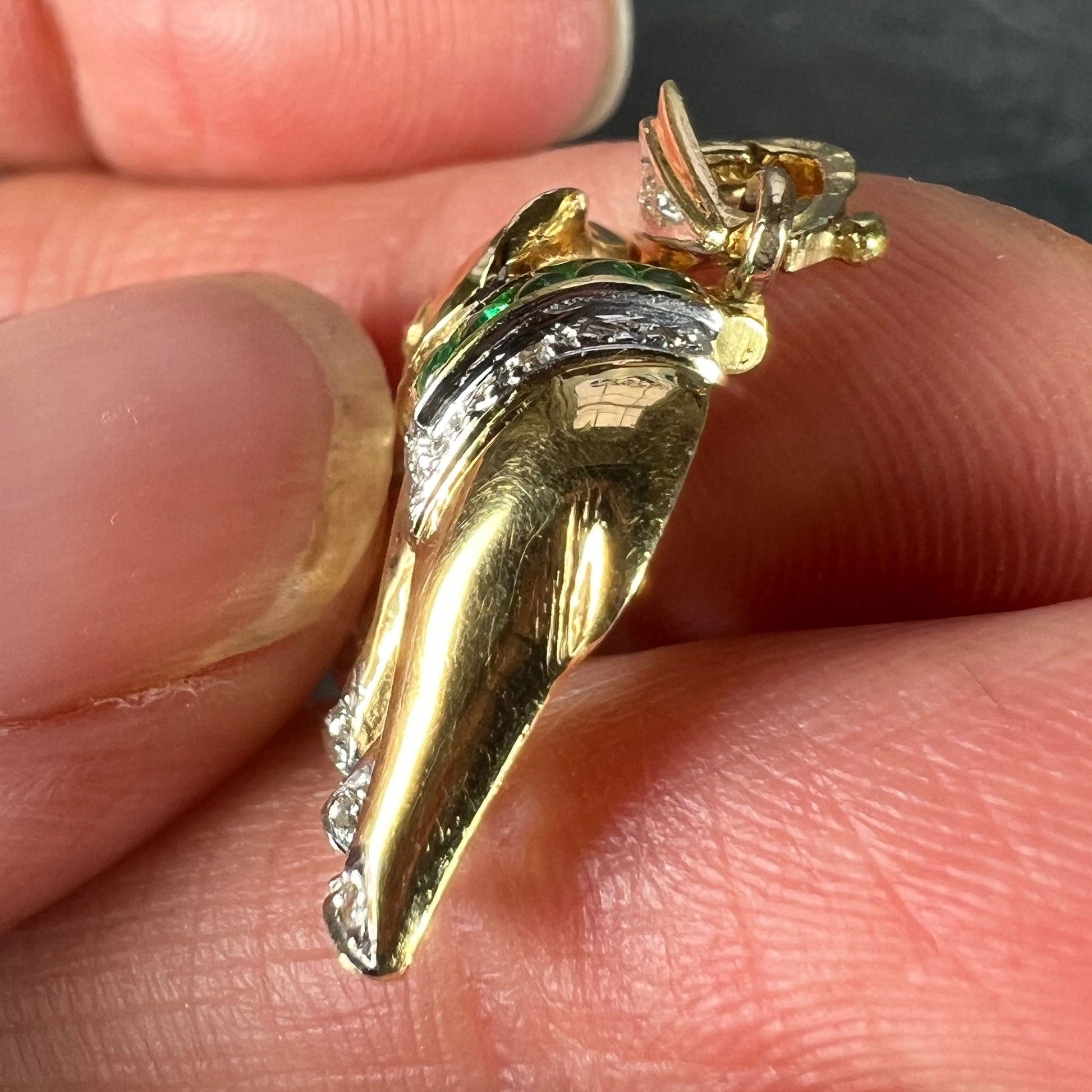 A yellow gold elephant pendant with rubies, emeralds and diamonds, held in a hand on a grey background