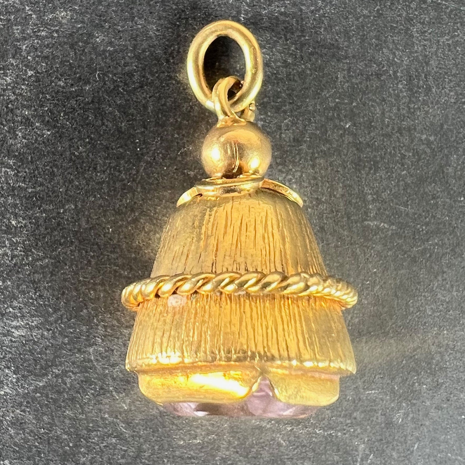 A yellow gold pendant with an amethyst set in the base, on a grey background