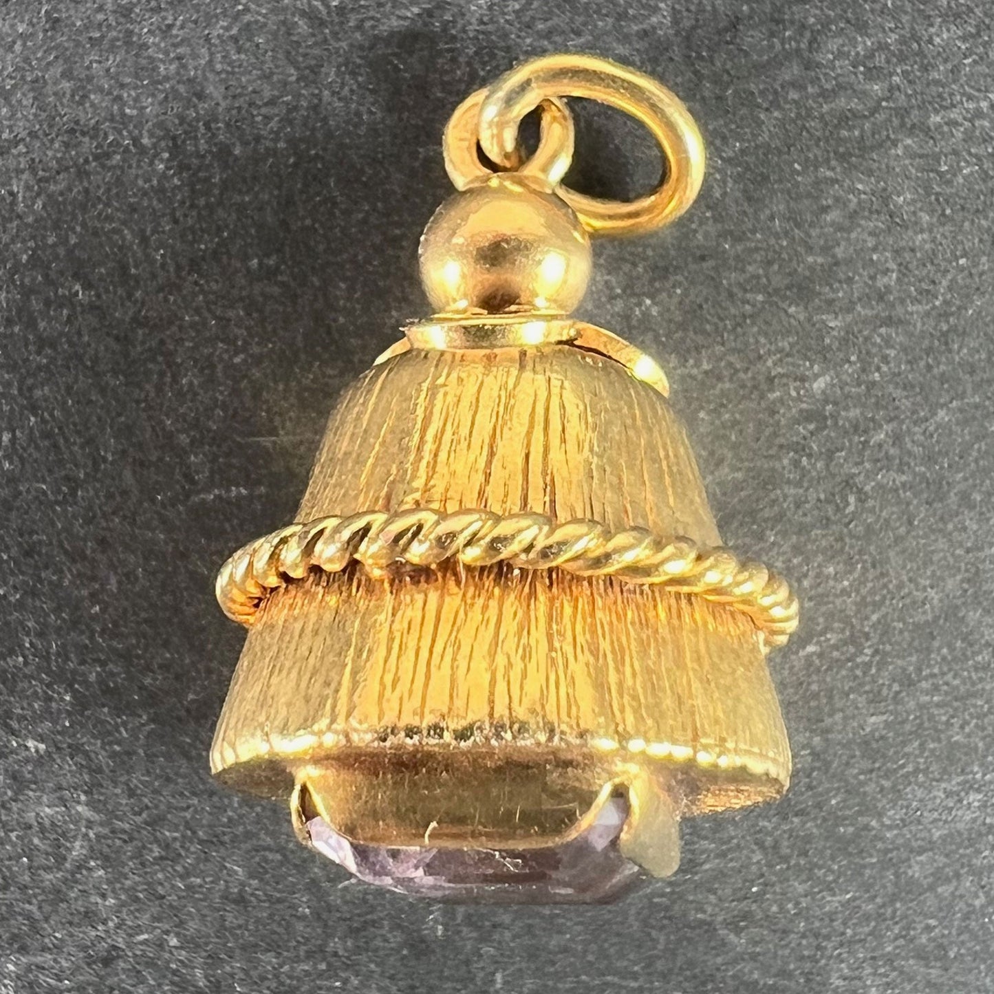 A yellow gold pendant with an amethyst set in the base, on a grey background