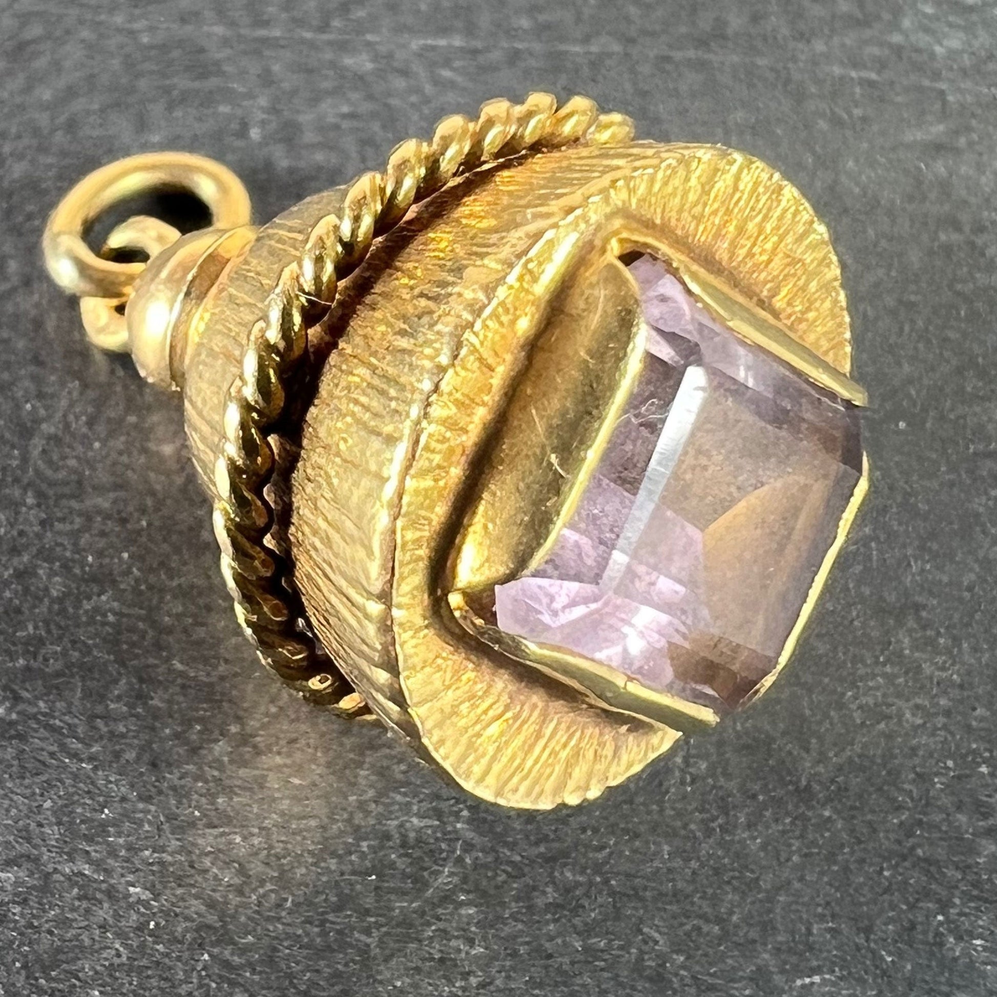A yellow gold pendant with an amethyst set in the base, on a grey background