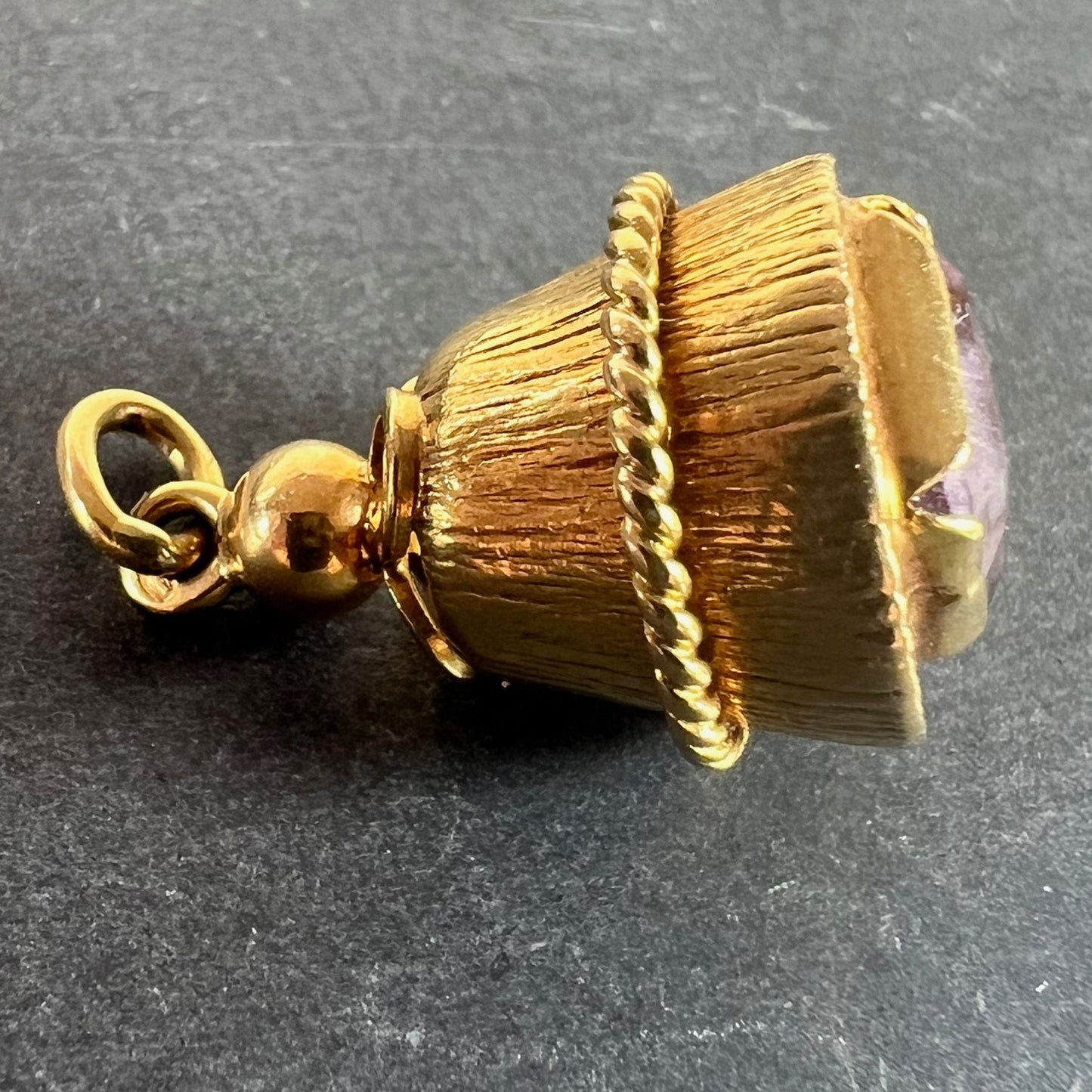 A yellow gold pendant with an amethyst set in the base, on a grey background