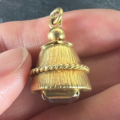 A yellow gold pendant with an amethyst set in the base, held in a hand on a grey background