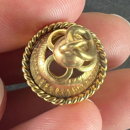 A yellow gold pendant, held in a hand on a grey background